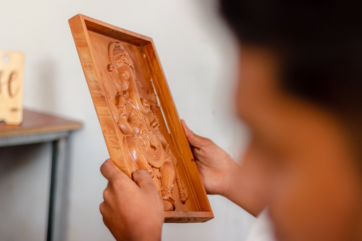 A maker inspecting a carved wooden panel by hand